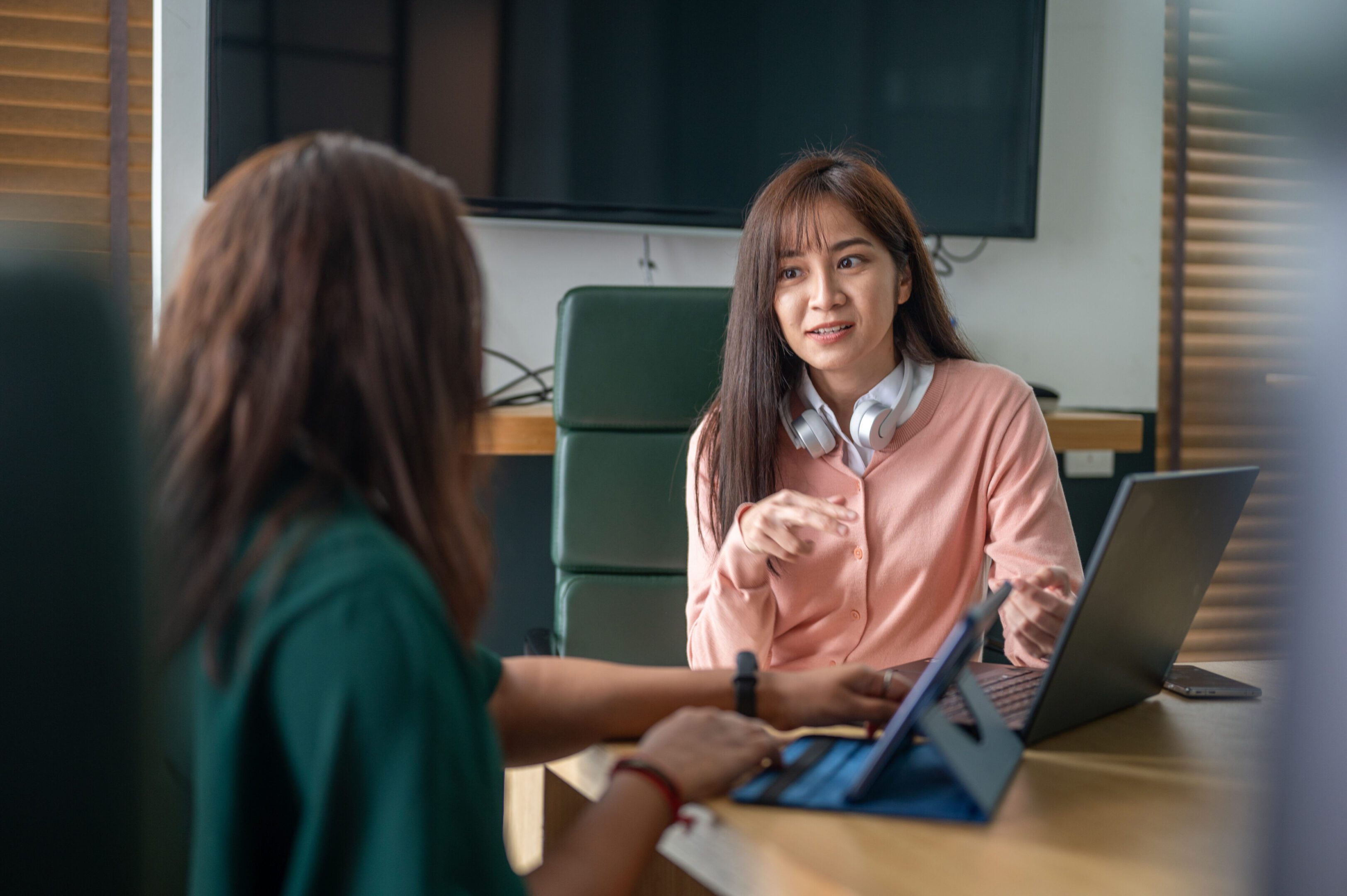 An Asian woman financial advisor is presenting ideas, plans, and direction to a woman investor in a modern conference room, collaborating creatively on project planning.